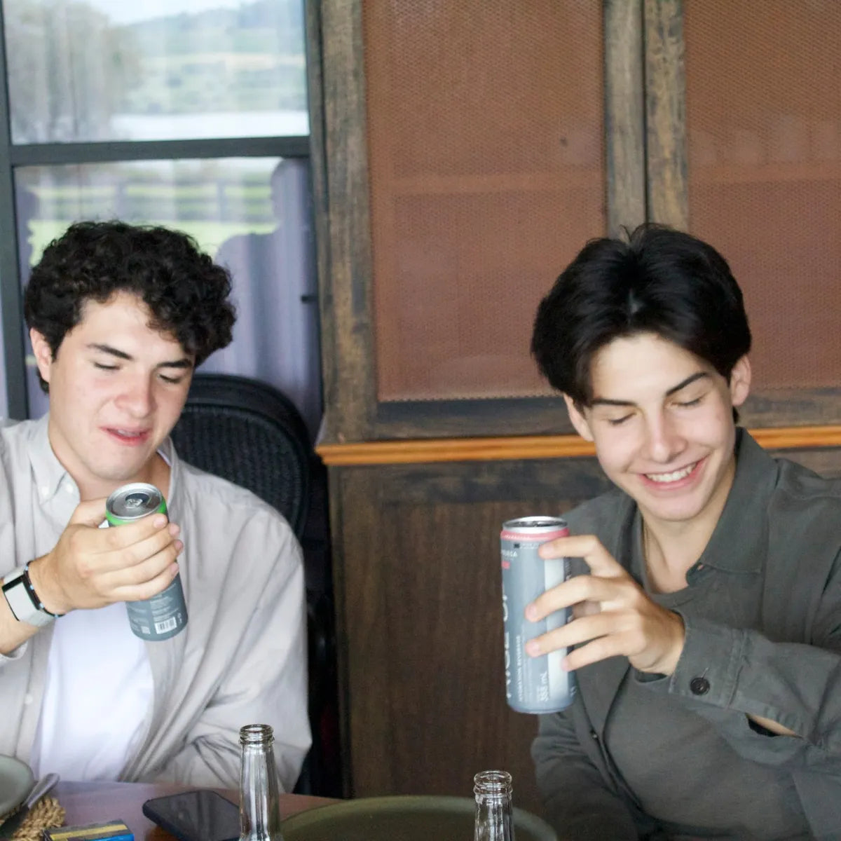 Dos amigos sentados a la mesa de un restaurante abriendo sus latas de Rise Up Citrus y Frambuesa